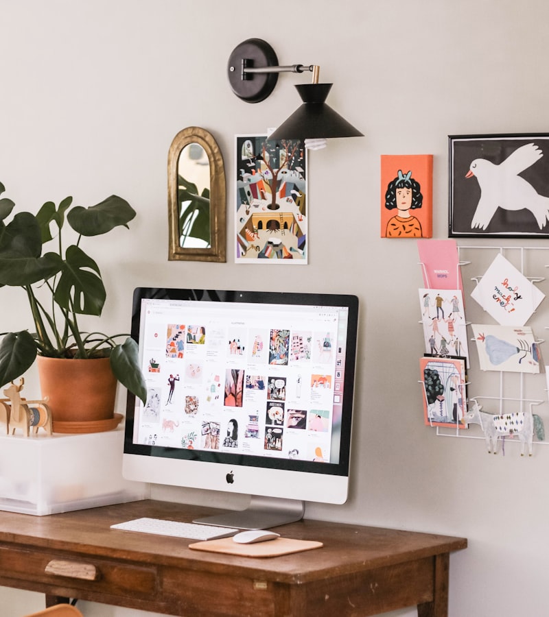 A bright home studio desk with a moodboard, plants and a computer